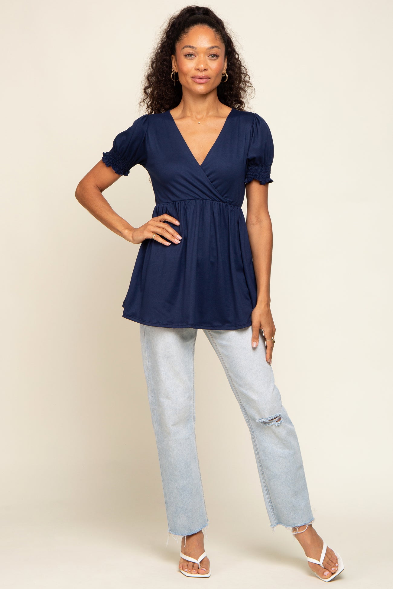 woman wearing a navy blue wrap top with puff sleeves paired with light wash distressed jeans