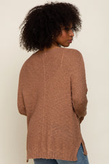 woman wearing a brown oversized knitted sweater with a textured finish and side slits, viewed from the back