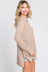 woman wearing a tan knit sweater with a relaxed fit and side slits, paired with denim shorts