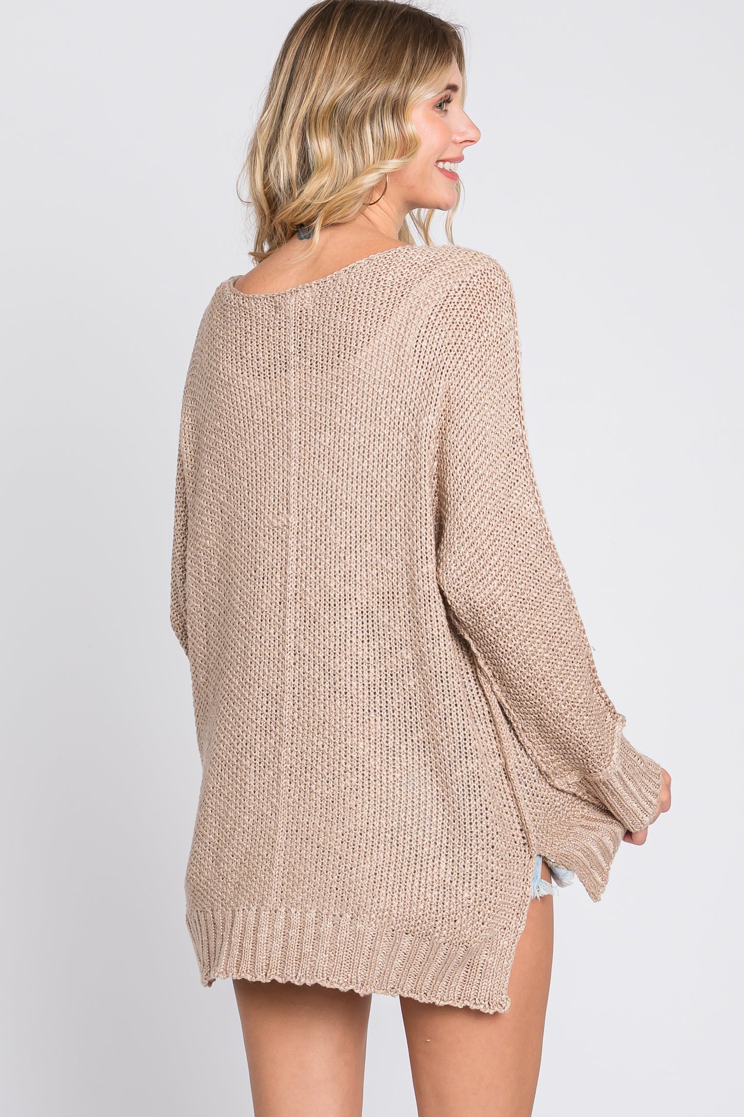 woman wearing a beige oversized knit sweater with a relaxed fit and open back detail