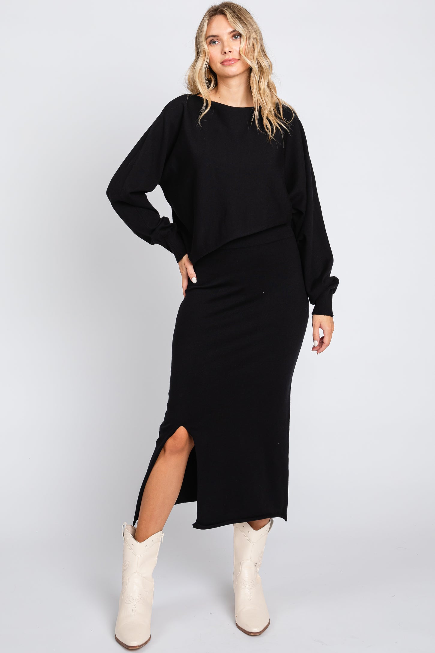 woman wearing a black cropped sweatshirt and a black midi skirt with a side slit, paired with white cowboy boots
