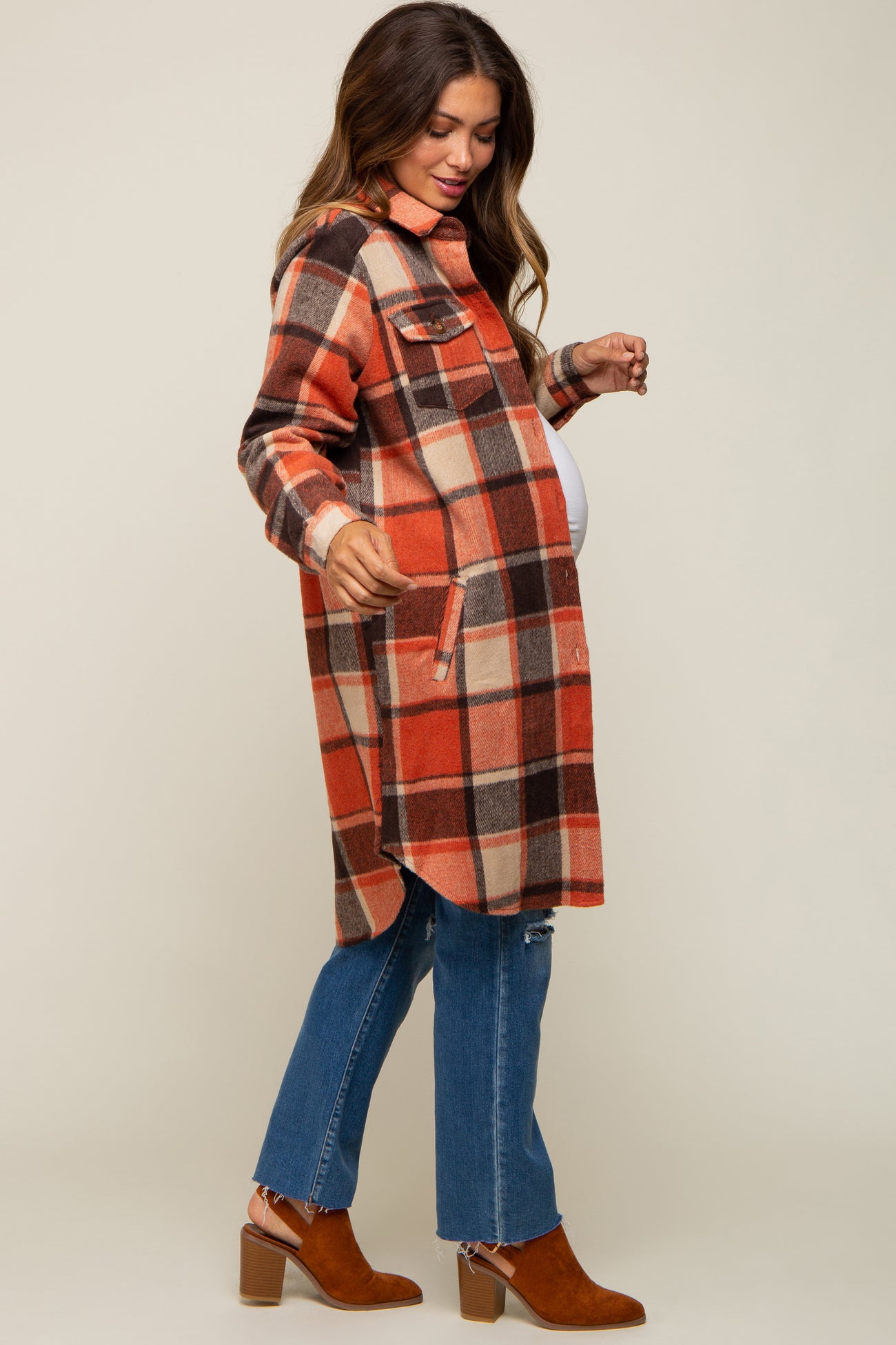 woman wearing a red and orange plaid maternity shacket with pockets and distressed jeans, showcasing her baby bump