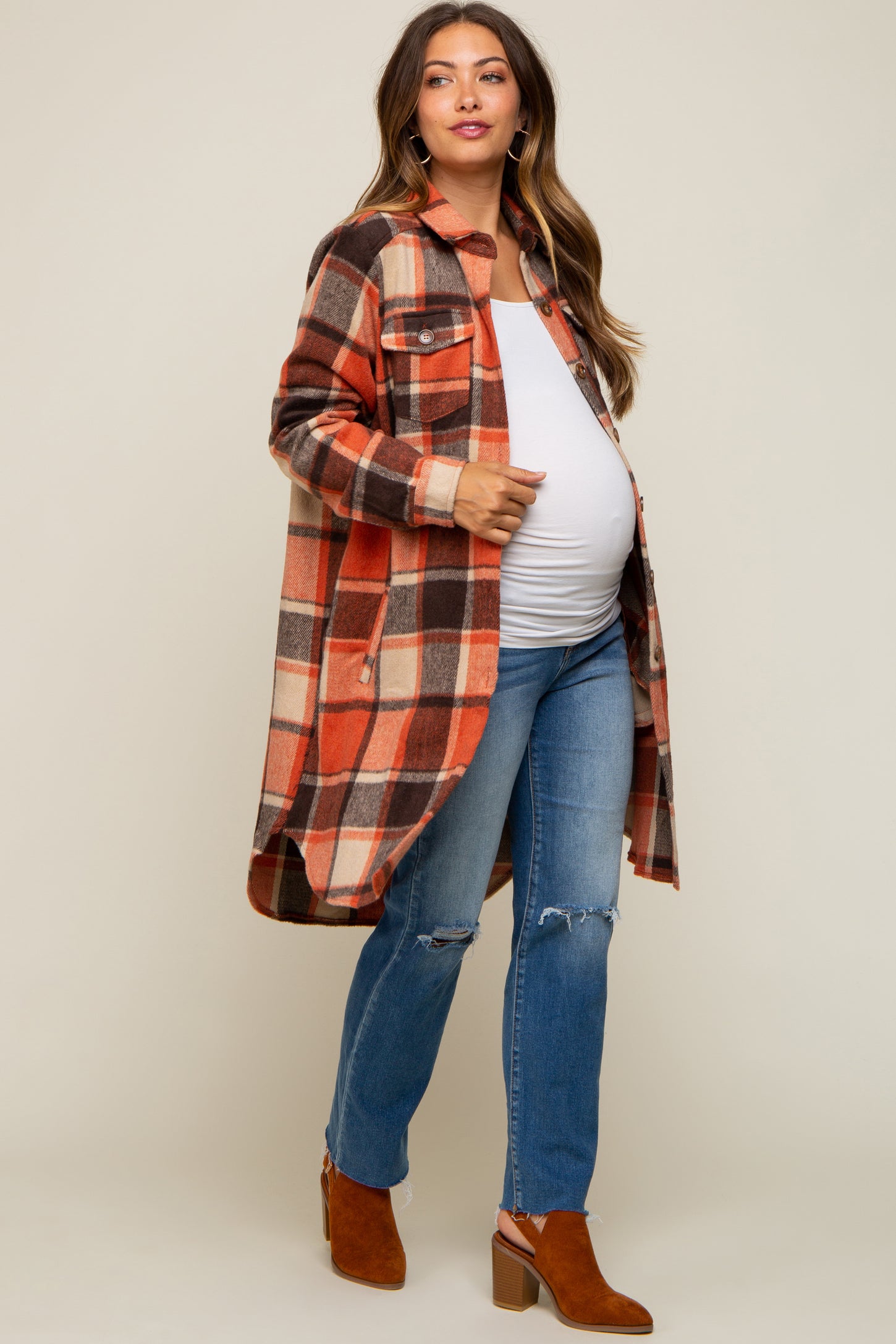 woman wearing an orange and brown plaid maternity shacket over a white top and blue jeans, showing her baby bump