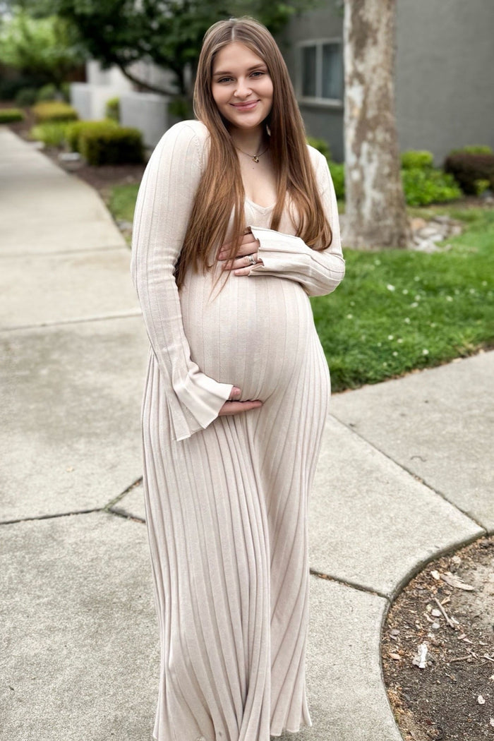 woman wearing a beige long sleeve maternity dress with ribbed texture, holding her baby bump outdoors