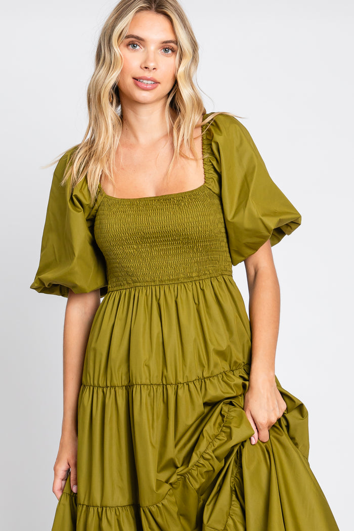 Woman wearing an olive green smocked midi dress with puff sleeves and a tiered skirt