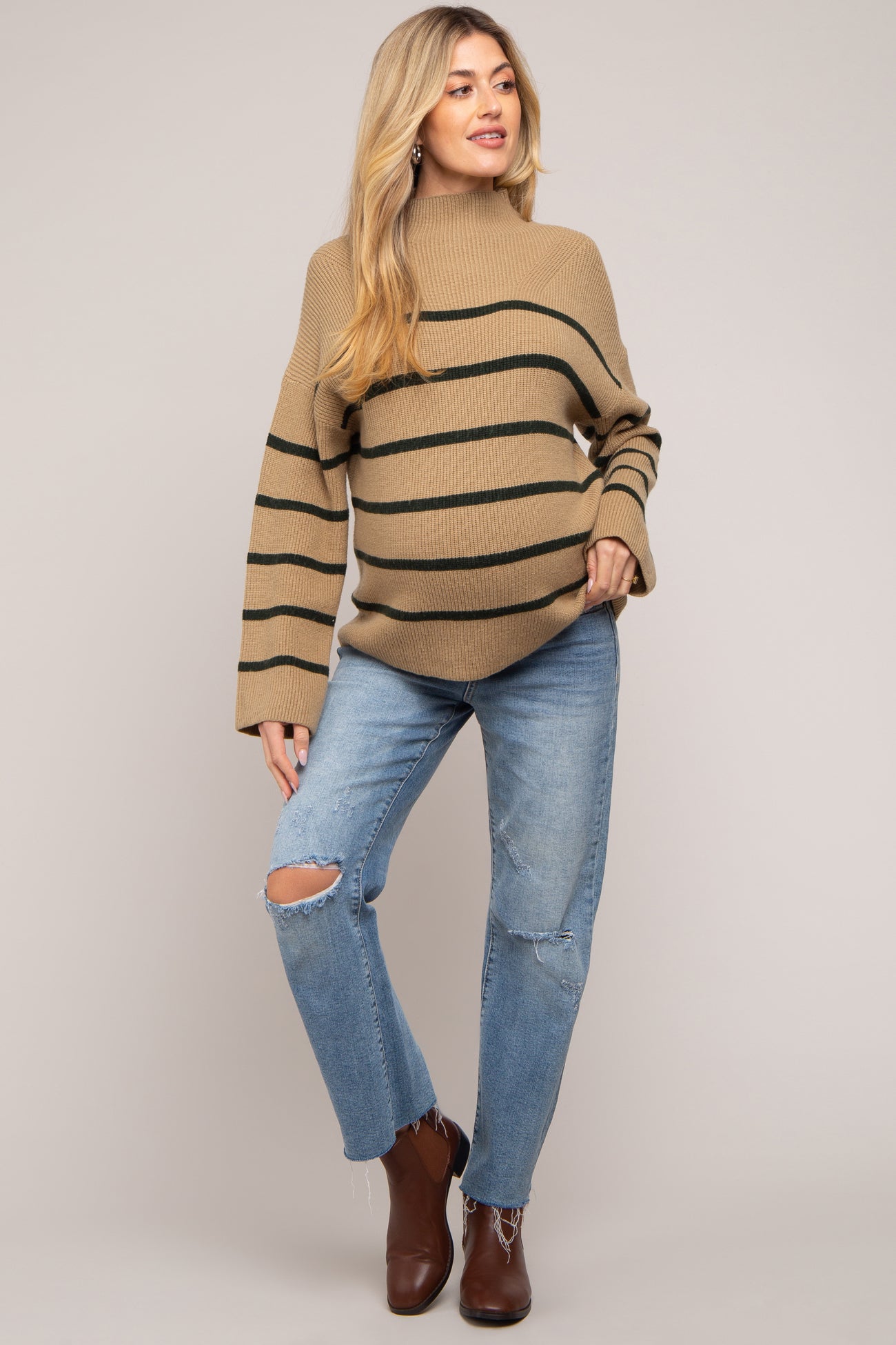 woman wearing a beige and green striped maternity sweater and distressed jeans, showing her baby bump
