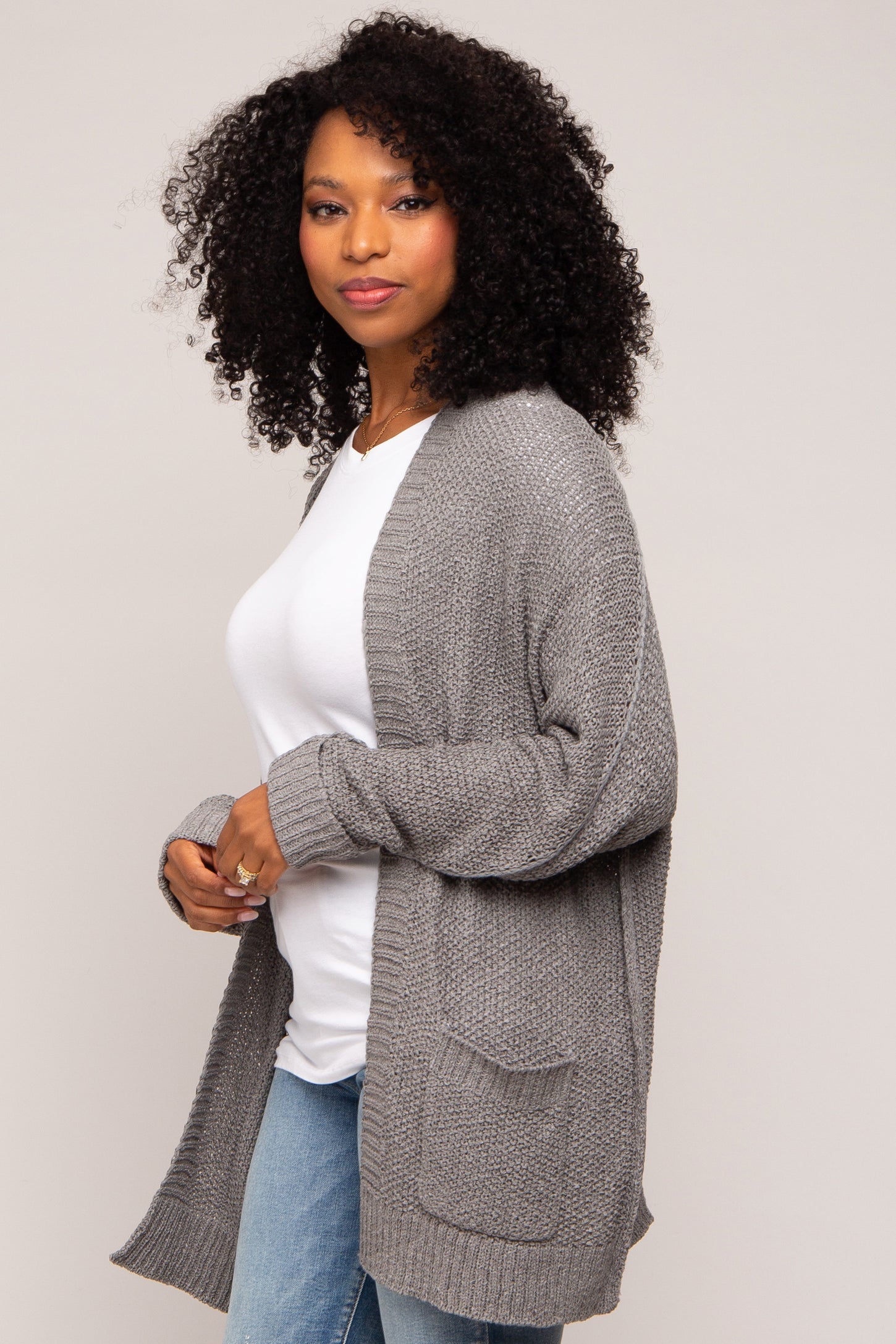 woman wearing a gray knitted cardigan over a white top and blue jeans, with curly hair styled down