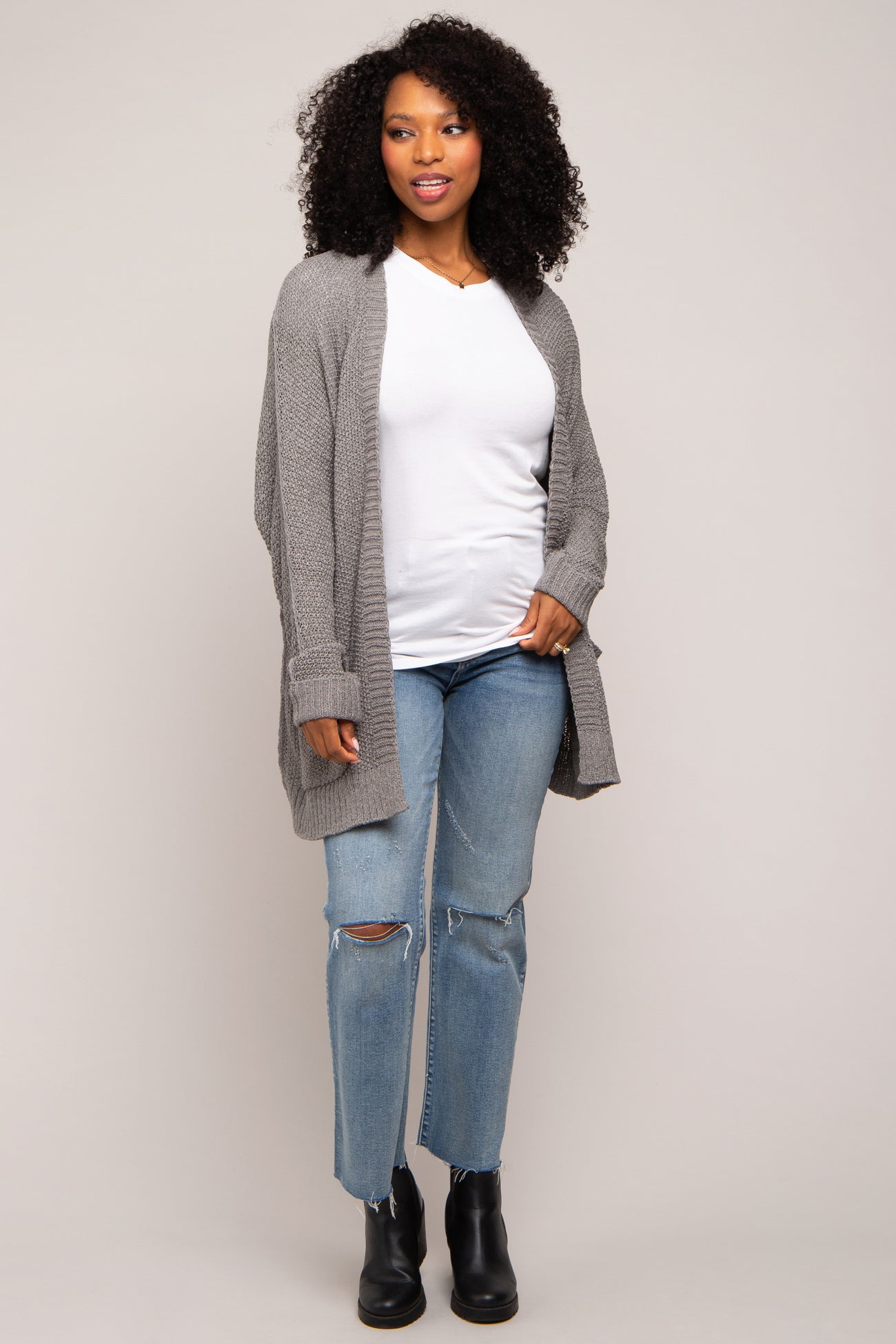 woman wearing a gray cardigan over a white top, paired with distressed jeans and black ankle boots