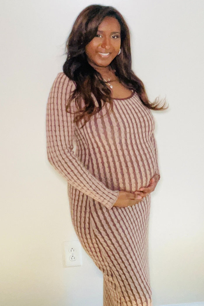 woman wearing a brown striped maternity dress and cradling her baby bump