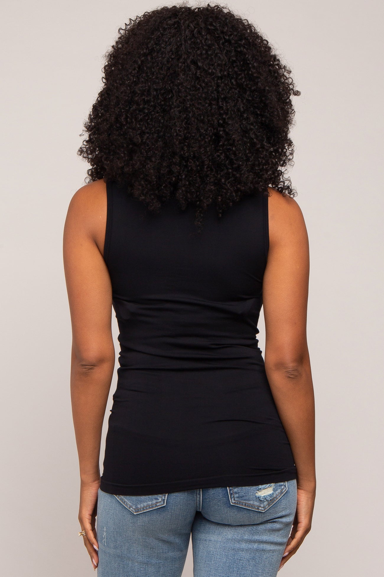 woman wearing a black sleeveless fitted top, viewed from the back, paired with light blue skinny jeans