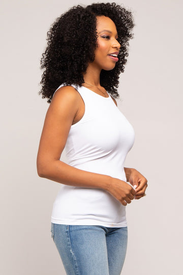woman wearing a white sleeveless tank top and light blue jeans, smiling and standing in profile