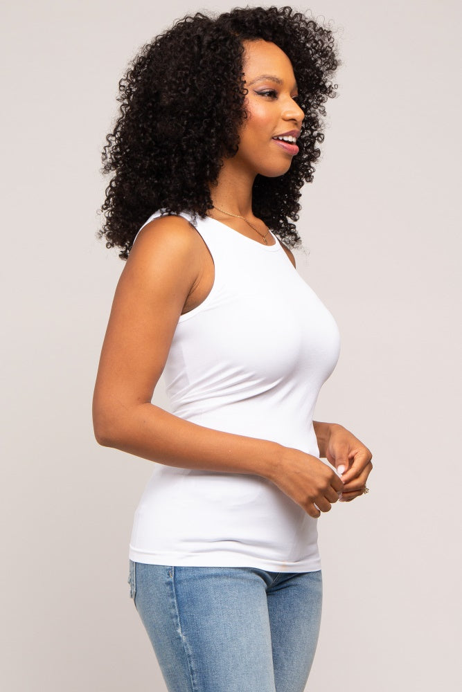 woman wearing a white sleeveless tank top and light blue jeans, smiling and standing in profile