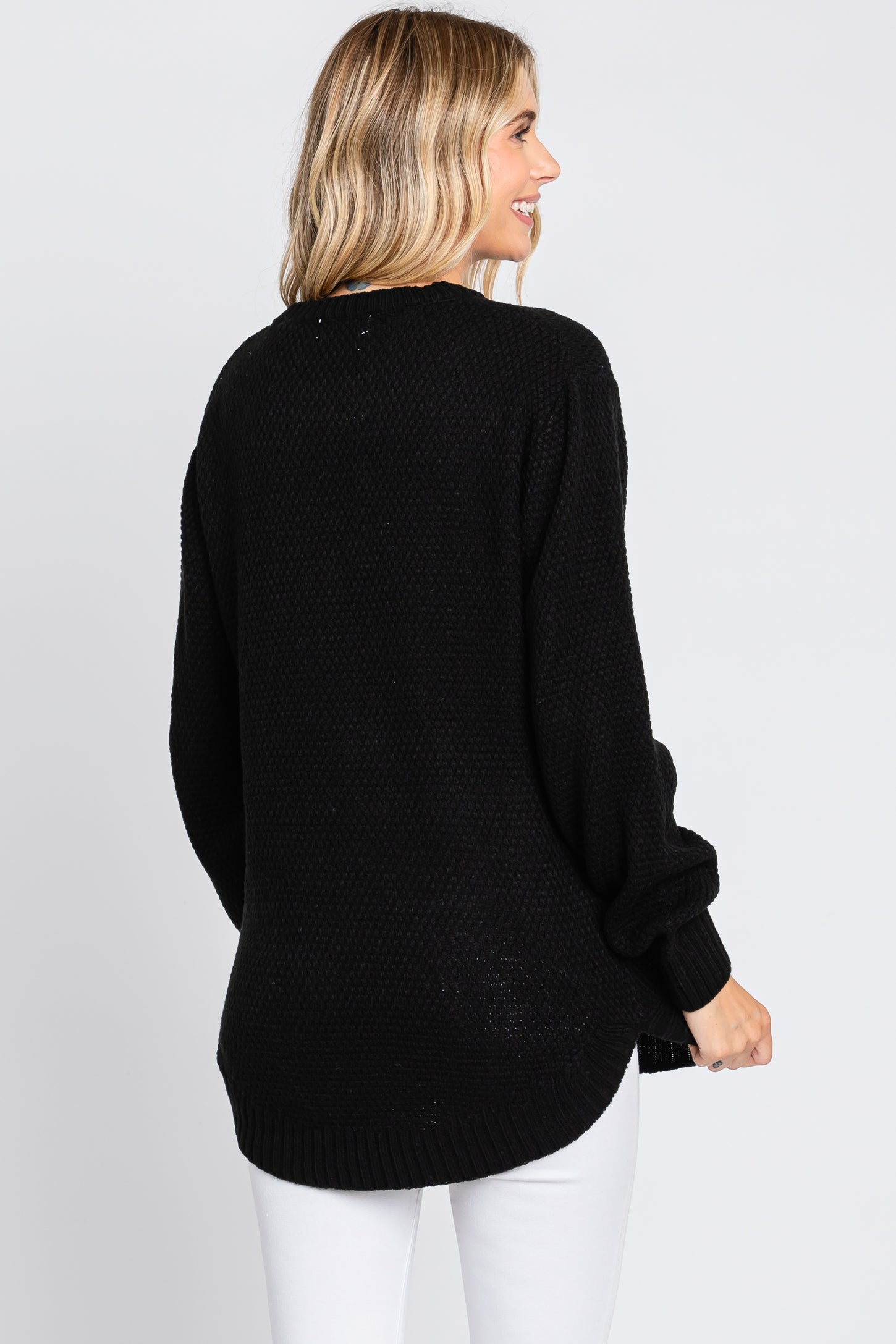 woman wearing a black oversized knit sweater with long sleeves and a curved hem, seen from the back