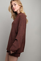 woman wearing a rust brown oversized knit sweater and matching shorts, styled casually with long wavy hair