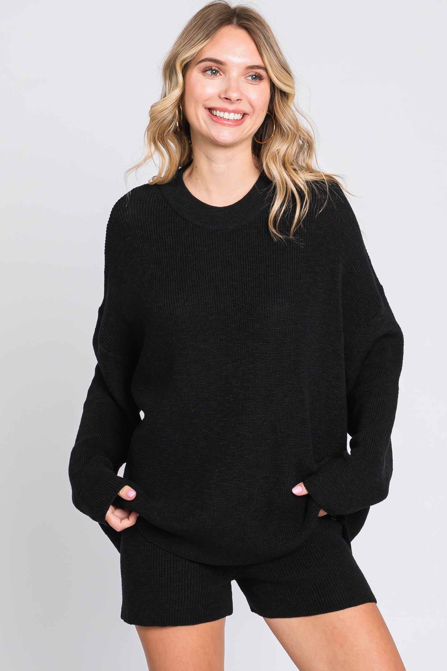 woman wearing a black oversized knit sweater and matching black shorts, smiling at the camera