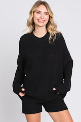 woman wearing a black oversized knit sweater and matching black shorts, smiling at the camera