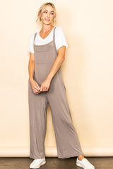woman wearing a taupe jumpsuit over a white t-shirt, standing with hands relaxed and smiling