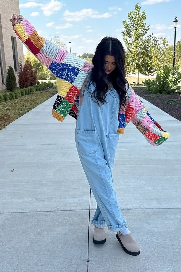 woman wearing a colorful knit cardigan over a light blue denim overall and beige slip-on shoes