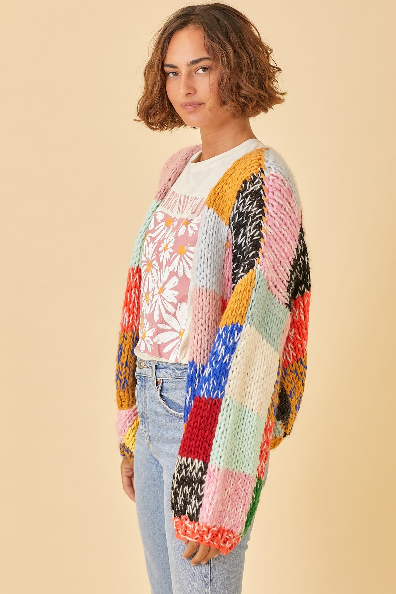 woman wearing a multicolored oversized knitted cardigan over a floral graphic tee and light wash jeans
