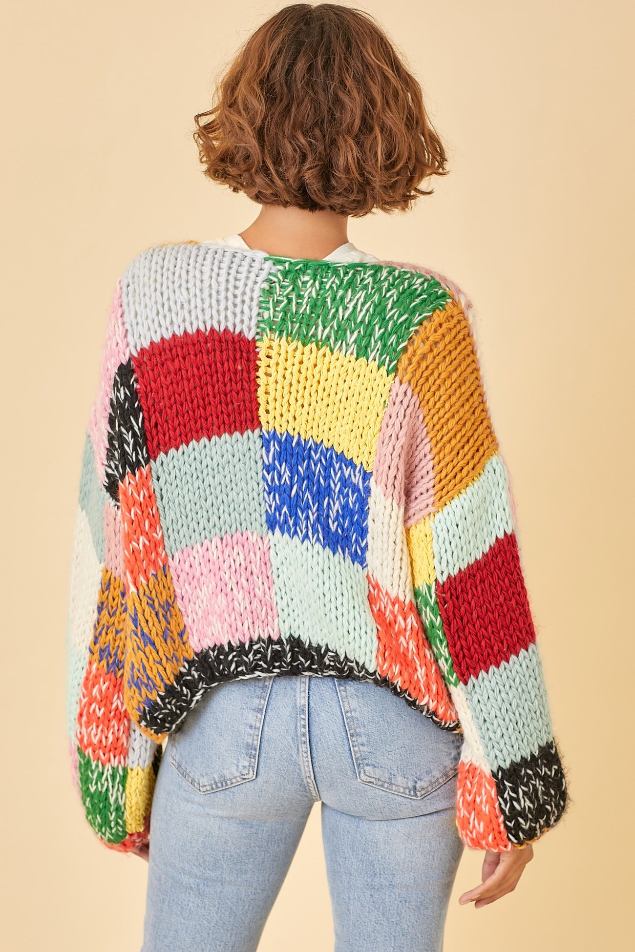 woman wearing a colorful oversized chunky knit sweater with a patchwork design, styled with high-waisted jeans