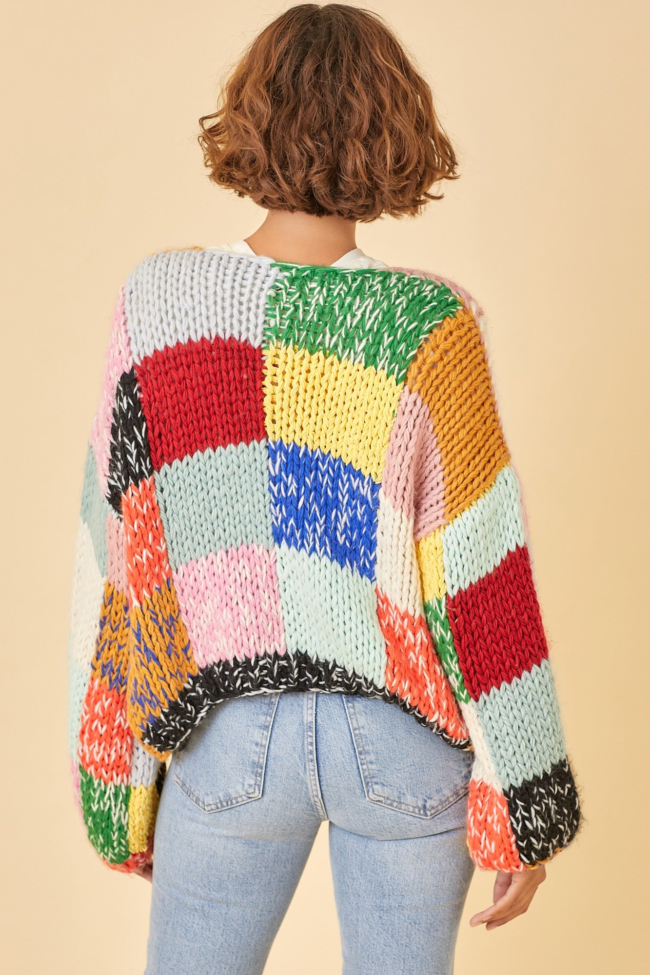 woman wearing a colorful oversized chunky knit sweater with a patchwork design, styled with high-waisted jeans