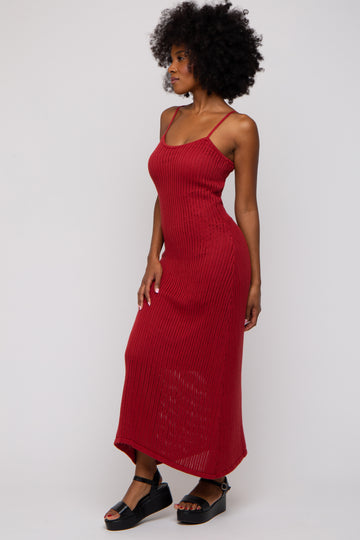 woman wearing a red ribbed maxi dress with thin straps and a fitted silhouette, standing in profile