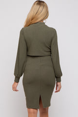 woman wearing a dark green ribbed maternity dress with a back slit and long puff sleeves