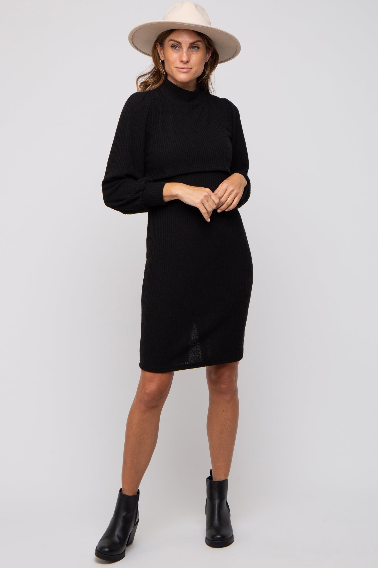 woman wearing a black ribbed long sleeve dress with a high neckline and ankle boots, accessorized with a wide-brimmed hat