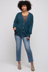 woman wearing a teal oversized cardigan with buttons, paired with a brown top and light blue jeans, styled with beige ankle boots
