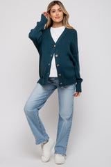 woman wearing a teal maternity cardigan over a white top and light blue jeans, standing in a casual pose