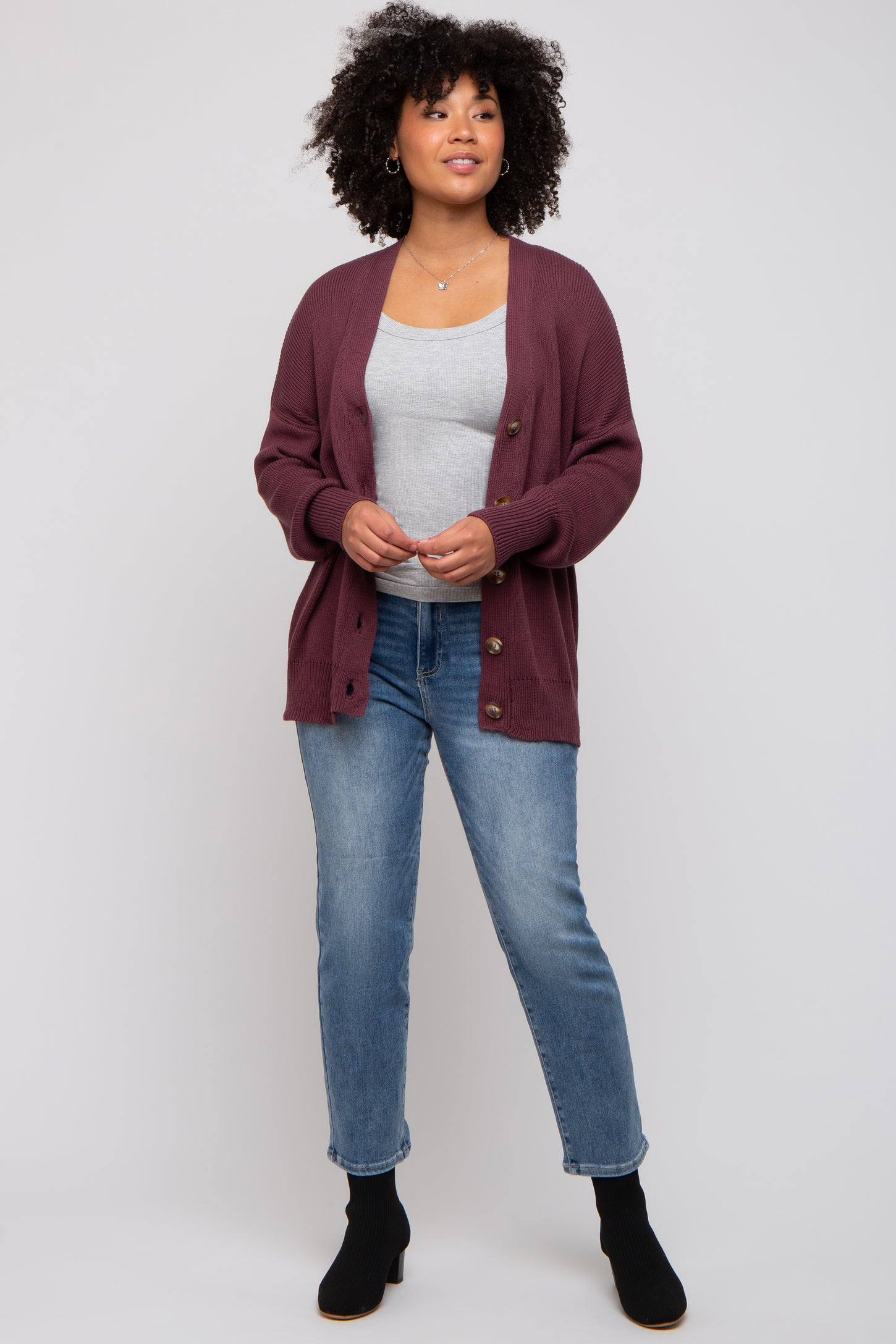 woman wearing a burgundy knitted cardigan over a grey top, paired with light blue jeans and black ankle boots