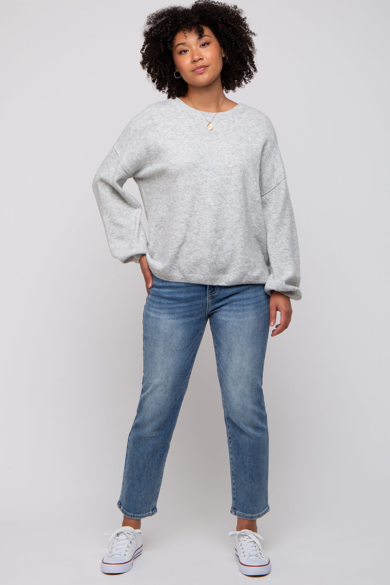 woman wearing a gray oversized sweatshirt with rolled sleeves and blue jeans, standing with a relaxed pose