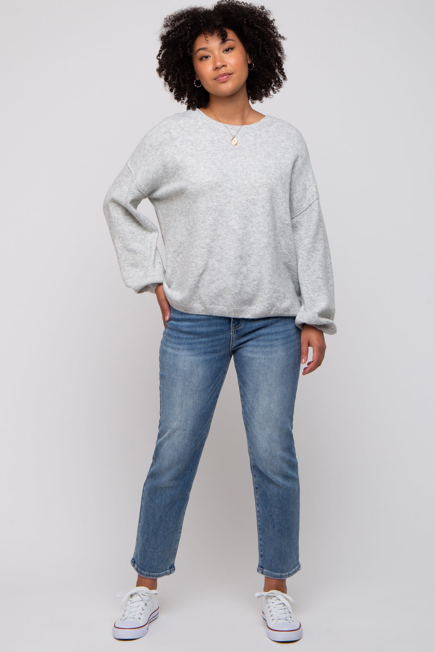woman wearing a gray oversized sweatshirt with rolled sleeves and blue jeans, standing with a relaxed pose