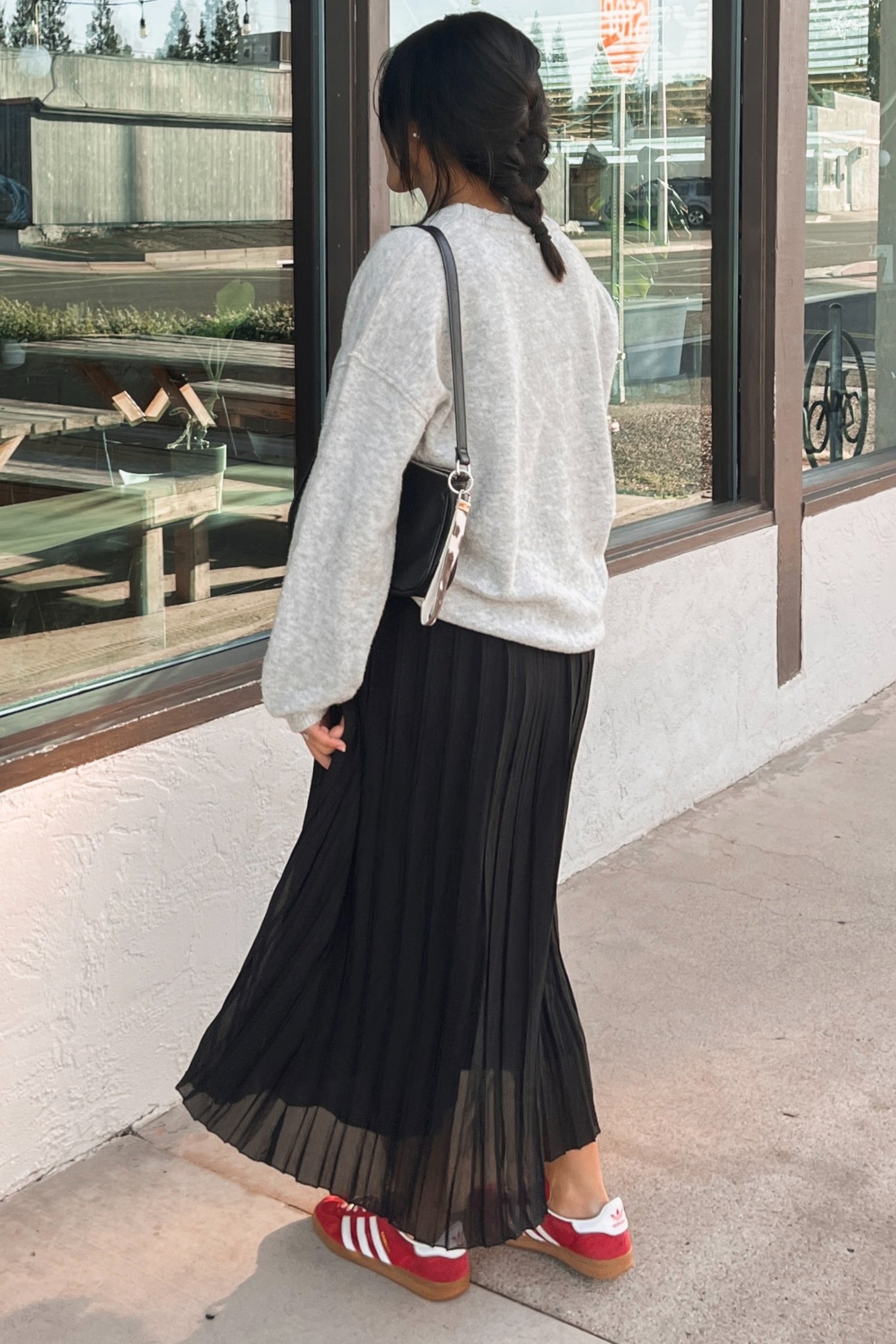 woman wearing a gray oversized sweatshirt and a black pleated maxi skirt, paired with red and white sneakers, standing outdoors
