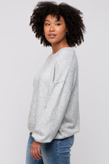woman wearing a light gray oversized sweater with a relaxed fit and dropped shoulders, paired with blue jeans