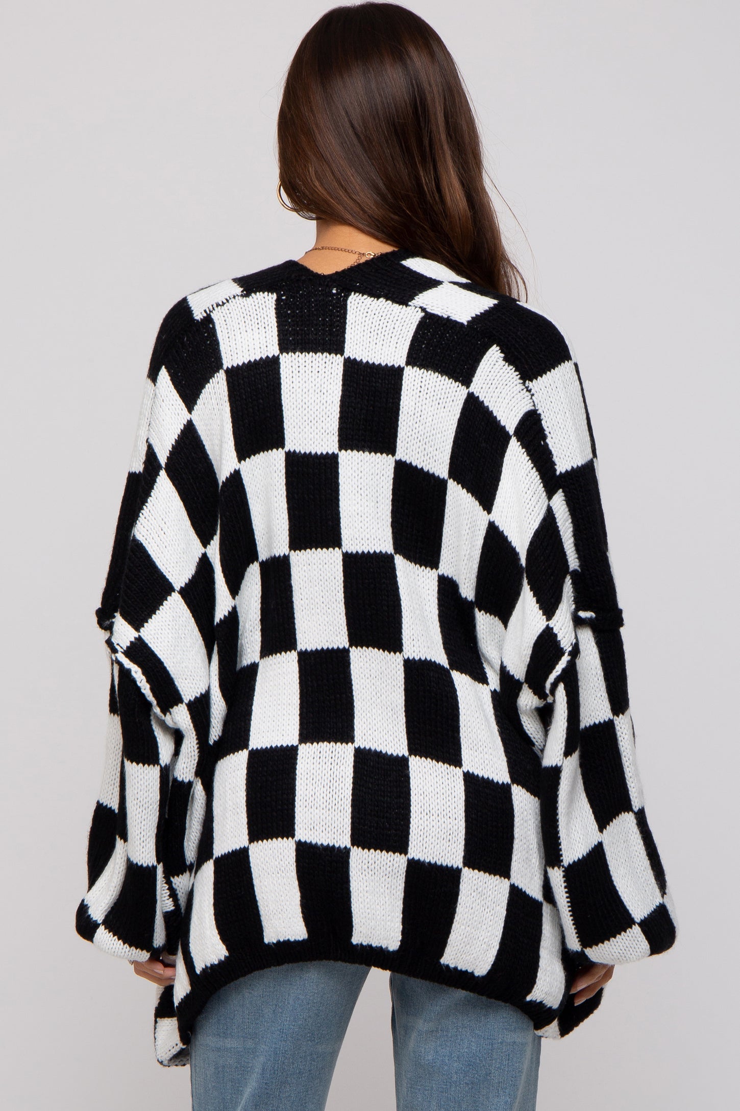 woman wearing a black and white checkered maternity sweater, with loose fit and open sleeves, viewed from the back