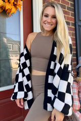 woman wearing a black and white checkered cardigan over a tan crop top and matching leggings, smiling at the camera