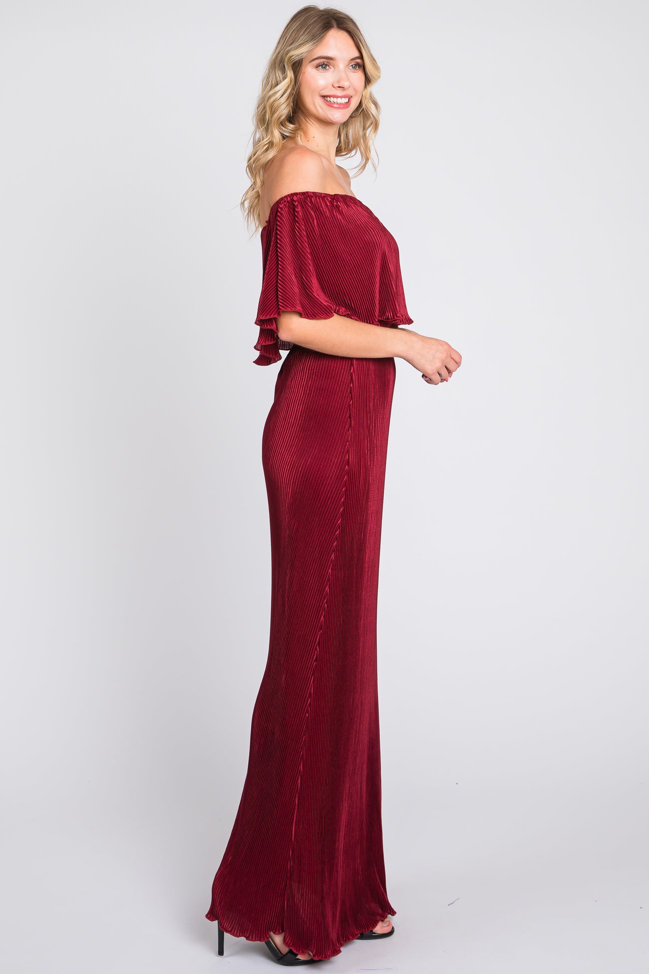 woman wearing a burgundy off-the-shoulder pleated maxi dress with ruffled sleeves standing in profile
