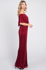 woman wearing a burgundy off-the-shoulder pleated maxi dress with ruffled sleeves standing in profile