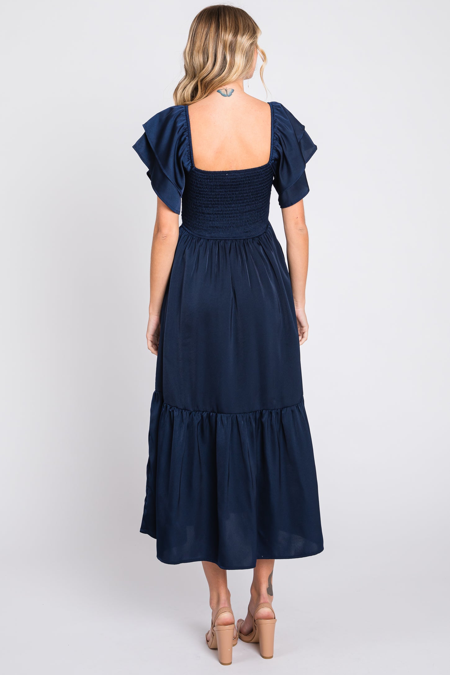 woman wearing a navy blue midi dress with short flutter sleeves and a smocked bodice, viewed from the back