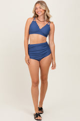 woman wearing a navy blue bikini with scalloped details and high-waisted bottoms, smiling on a neutral background