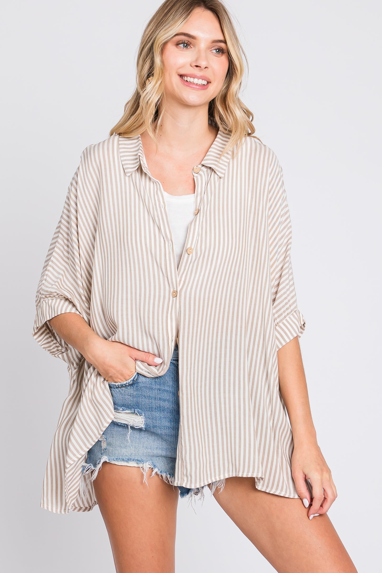 woman wearing a beige and cream striped oversized button-up shirt with rolled sleeves and denim shorts