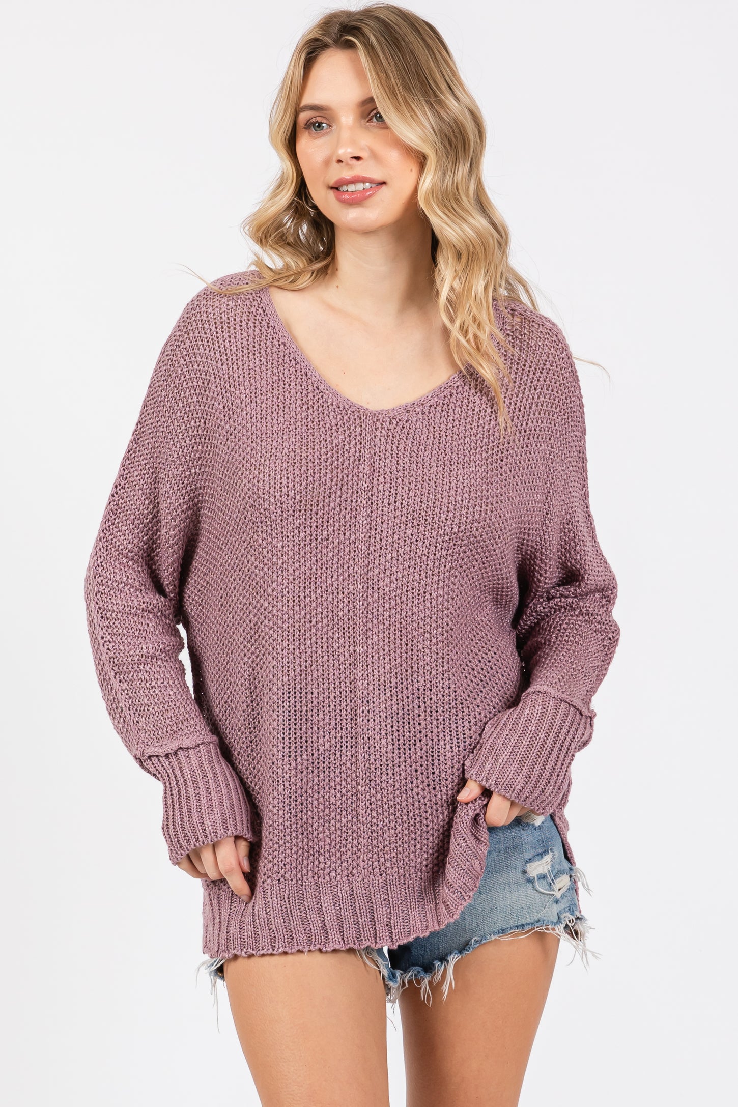 woman wearing a loose-fitting dusty pink knitted sweater with a v-neck and rolled cuffs, paired with denim shorts