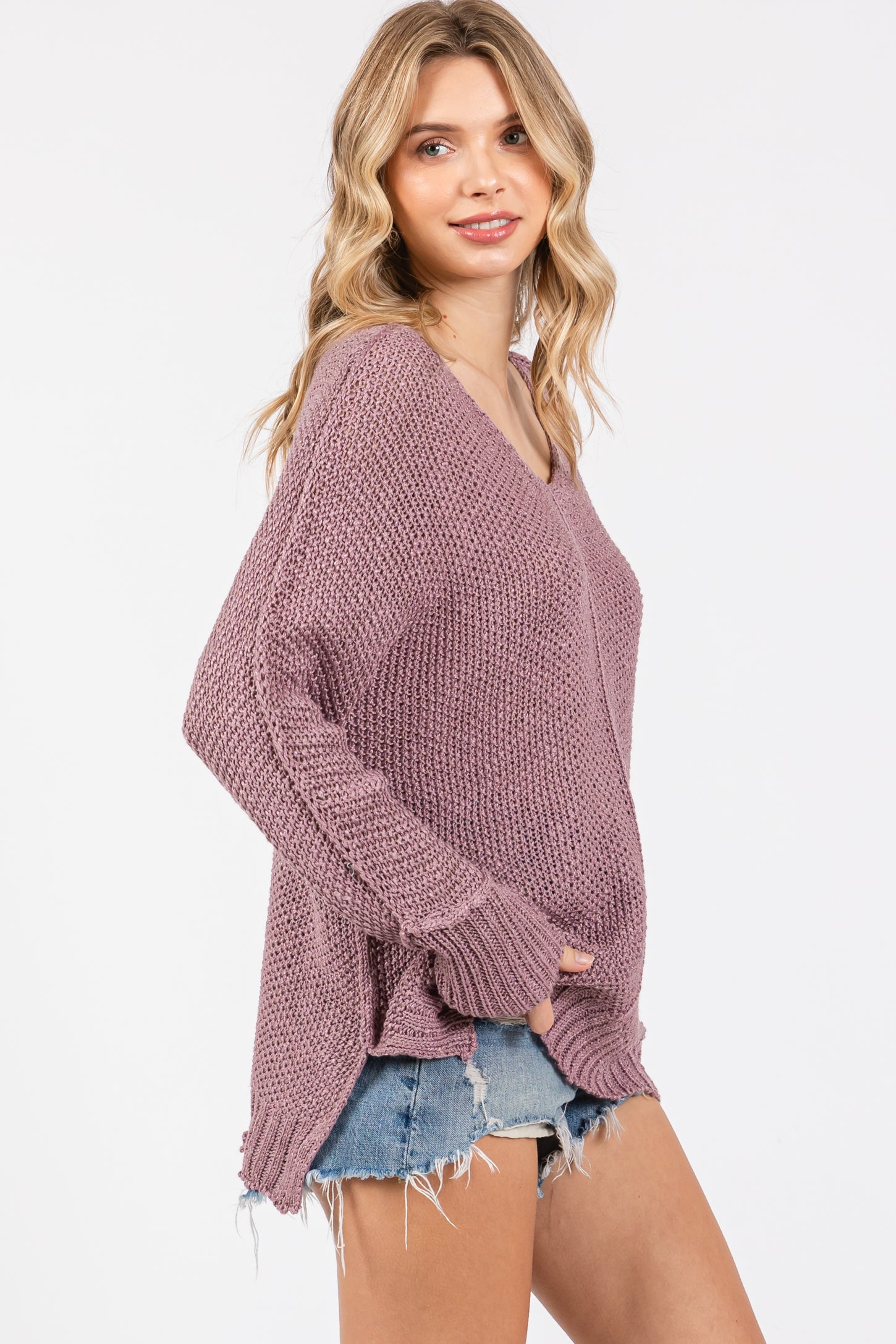 woman wearing a loose-fitting dusty pink v-neck sweater with frayed hem and denim shorts