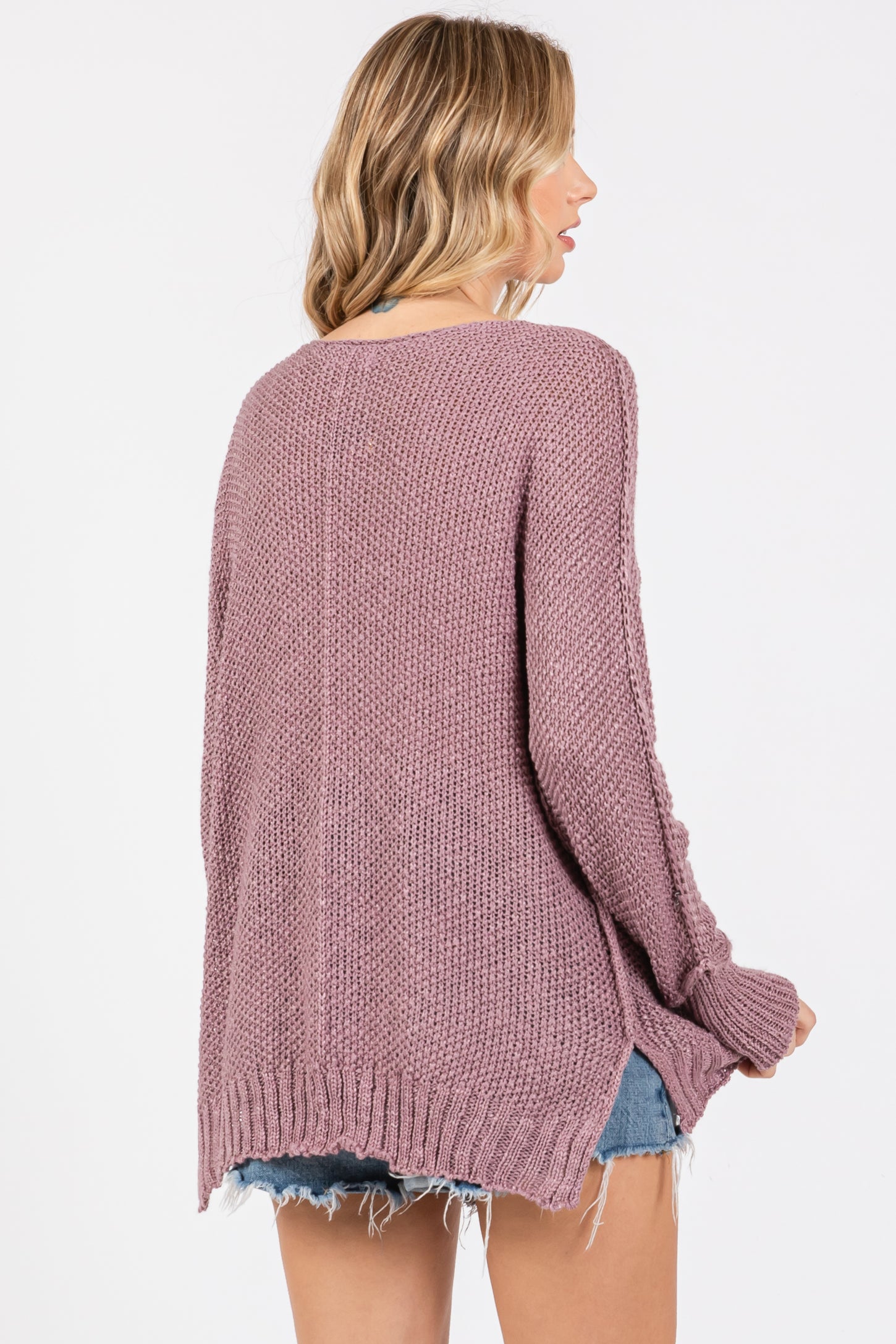 woman wearing a loose-fitting mauve knit sweater with side slits and a relaxed fit, styled with denim cut-off shorts