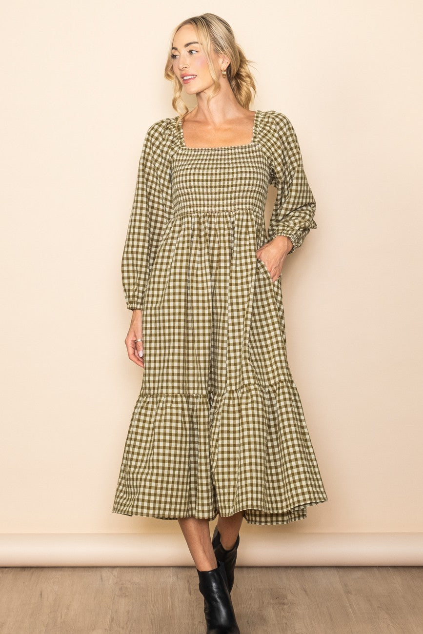 woman wearing a green and beige plaid midi dress with long sleeves and a tiered skirt, standing against a neutral background