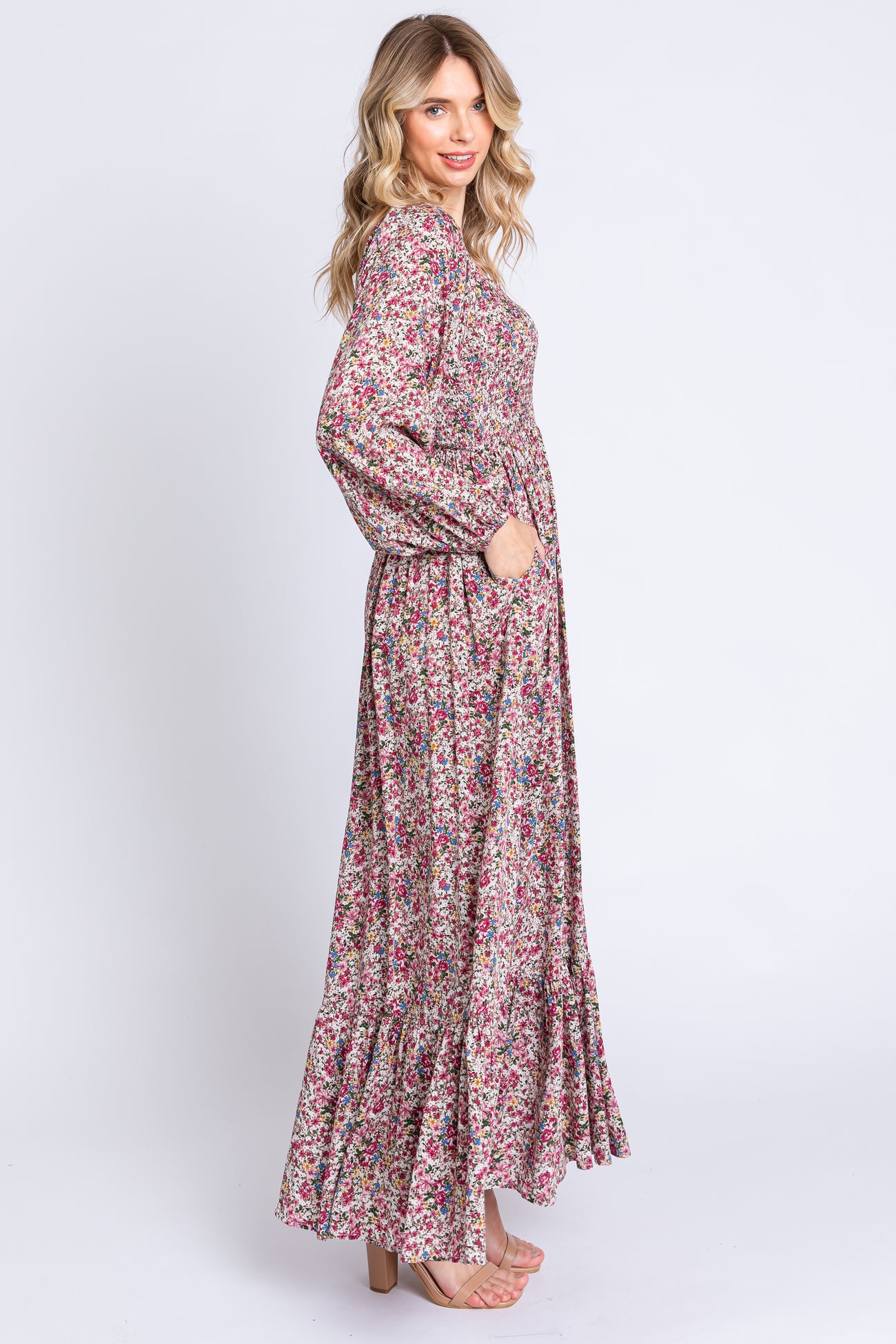 woman wearing a long floral print maxi dress with long sleeves and a ruffled hem, posing with her hands in pockets