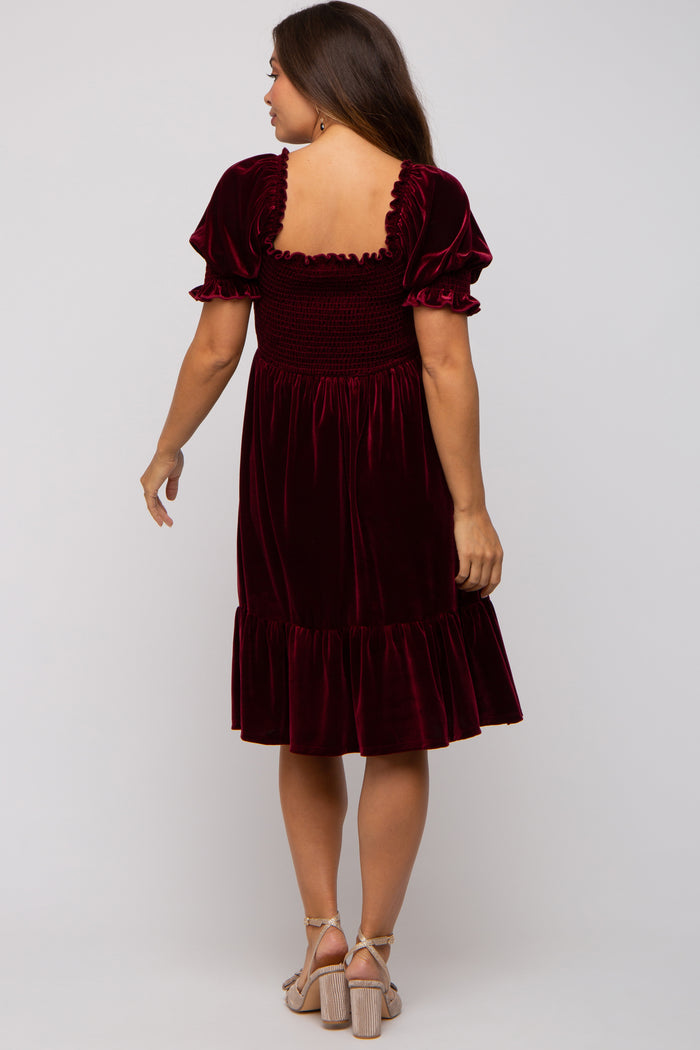 woman wearing a burgundy velvet maternity dress with puff sleeves and a ruffled hem, showing her back