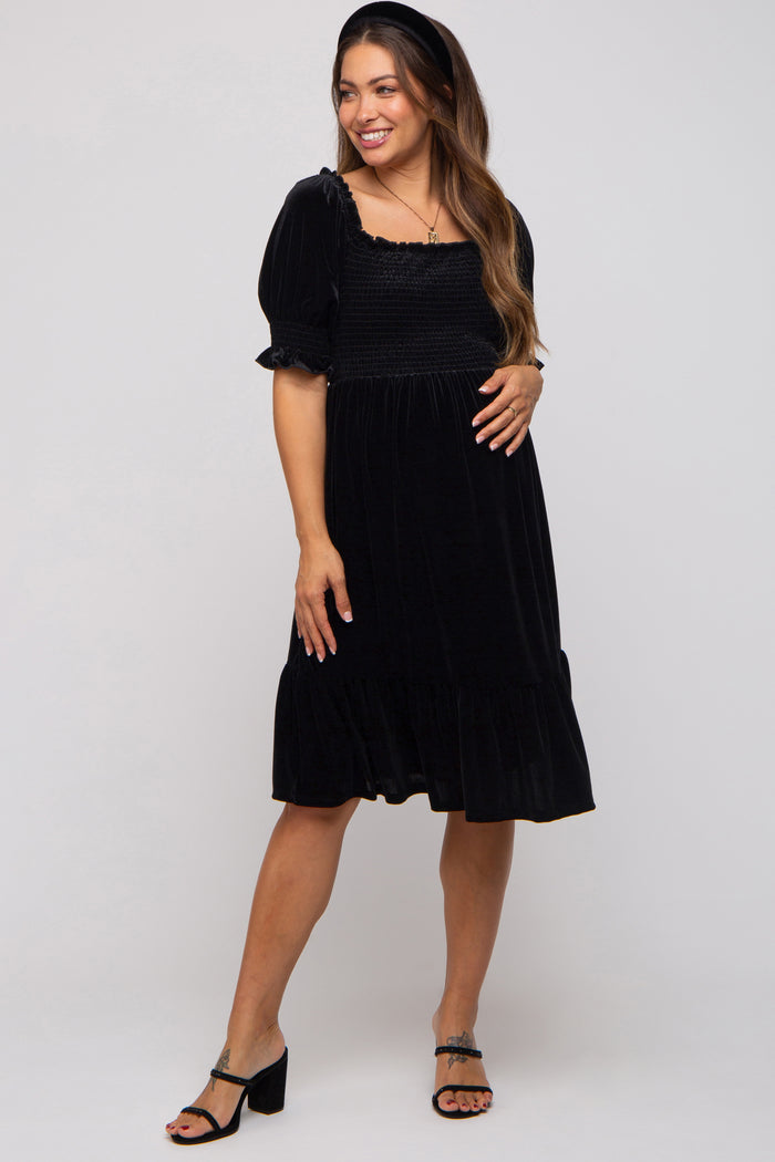 woman wearing a black maternity dress with puff sleeves and a smocked bodice, gently holding her baby bump