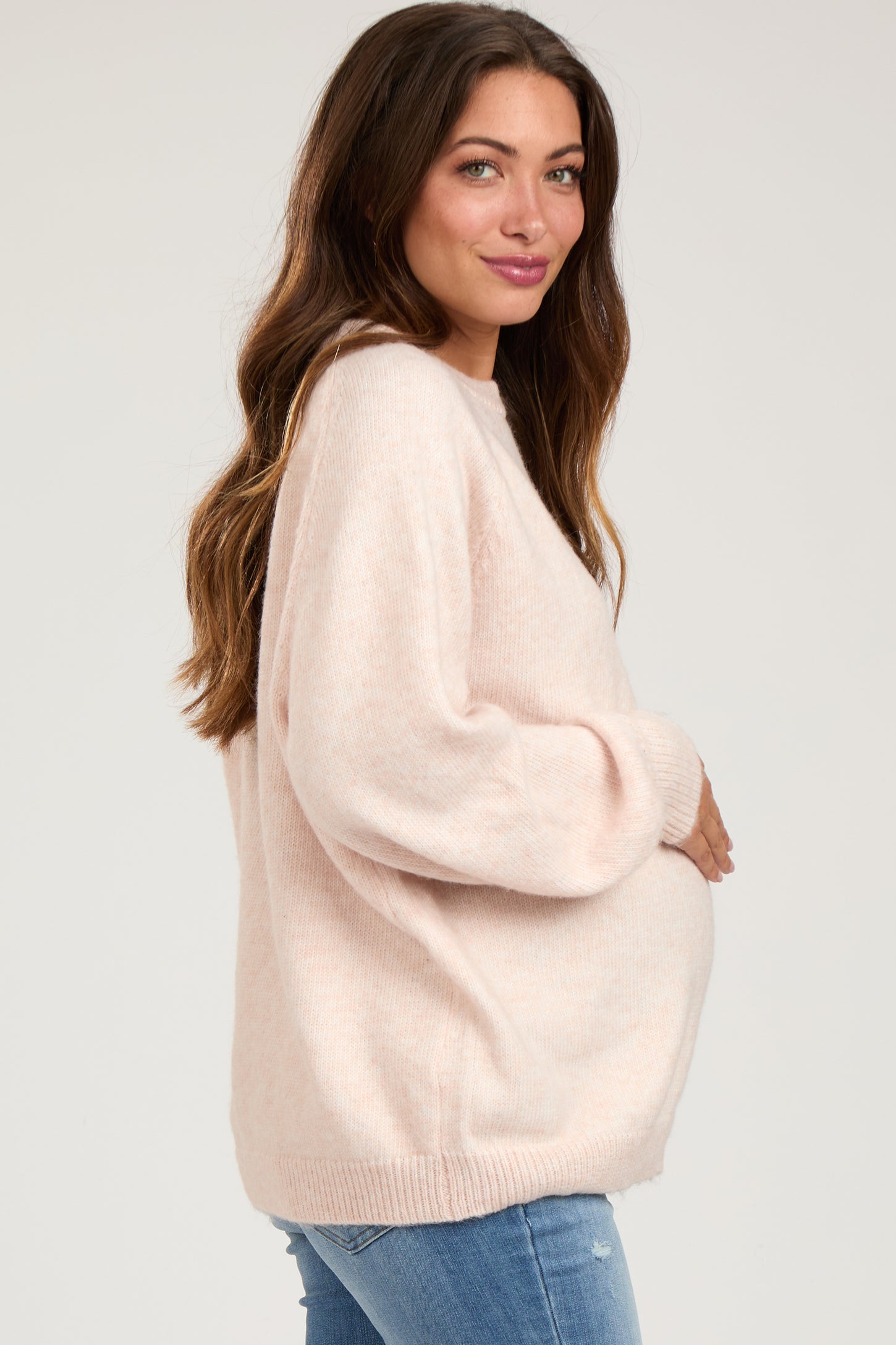 woman wearing a soft pink oversized maternity sweater and holding her baby bump